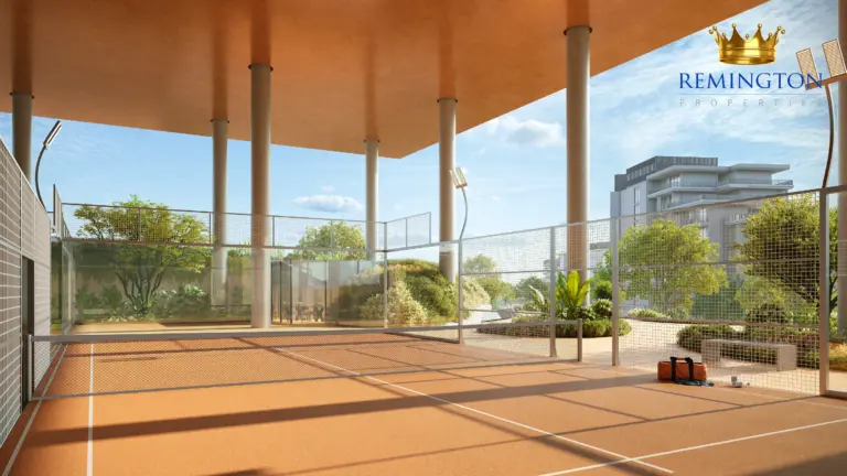 Glazed padel court with a net, shaded roof and views towards trees and nearby buildings